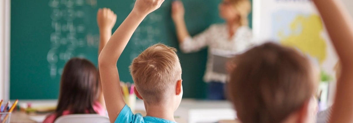 Een aantal kinderen in een klaslokaal, met leerkracht bij het bord